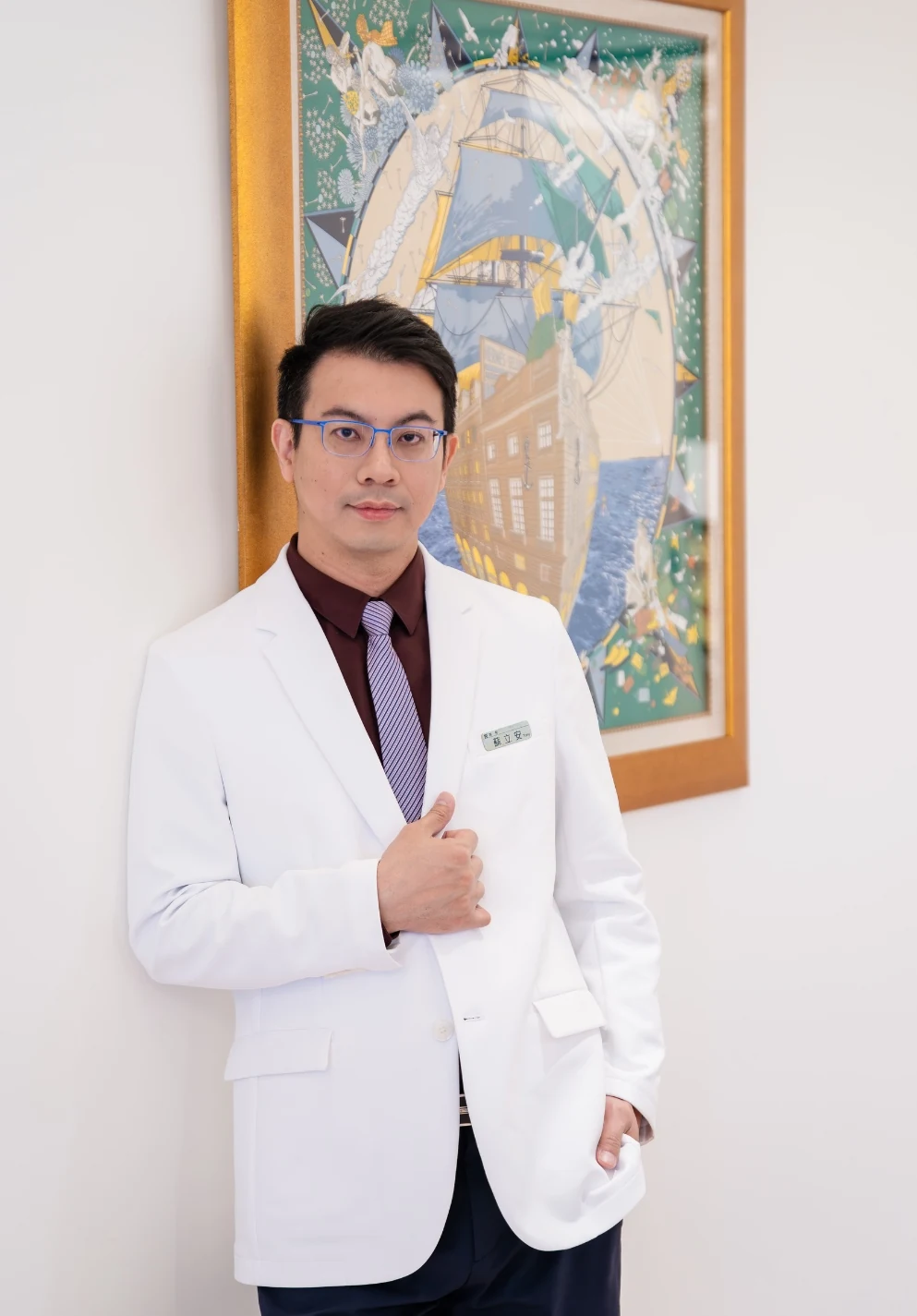Dr. Tony Su in a white physician's coat, calm and composed, standing before a framed artwork