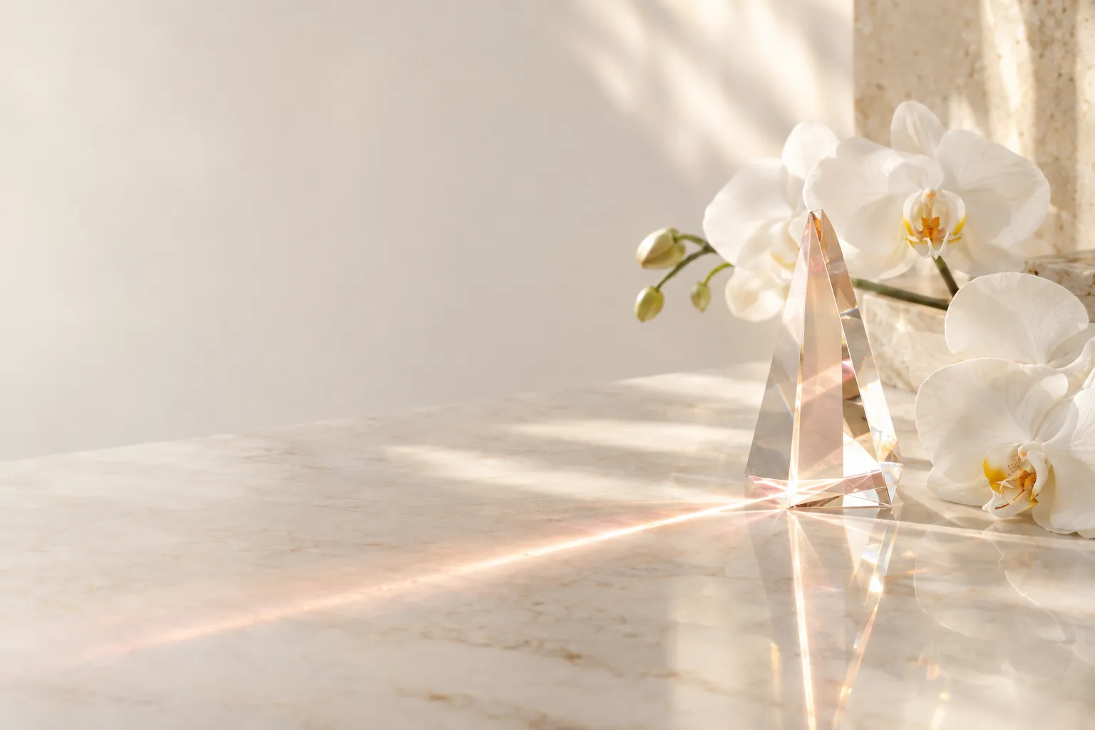 A soft beam of rose-gold light through a crystal prism on ivory marble beside white orchids