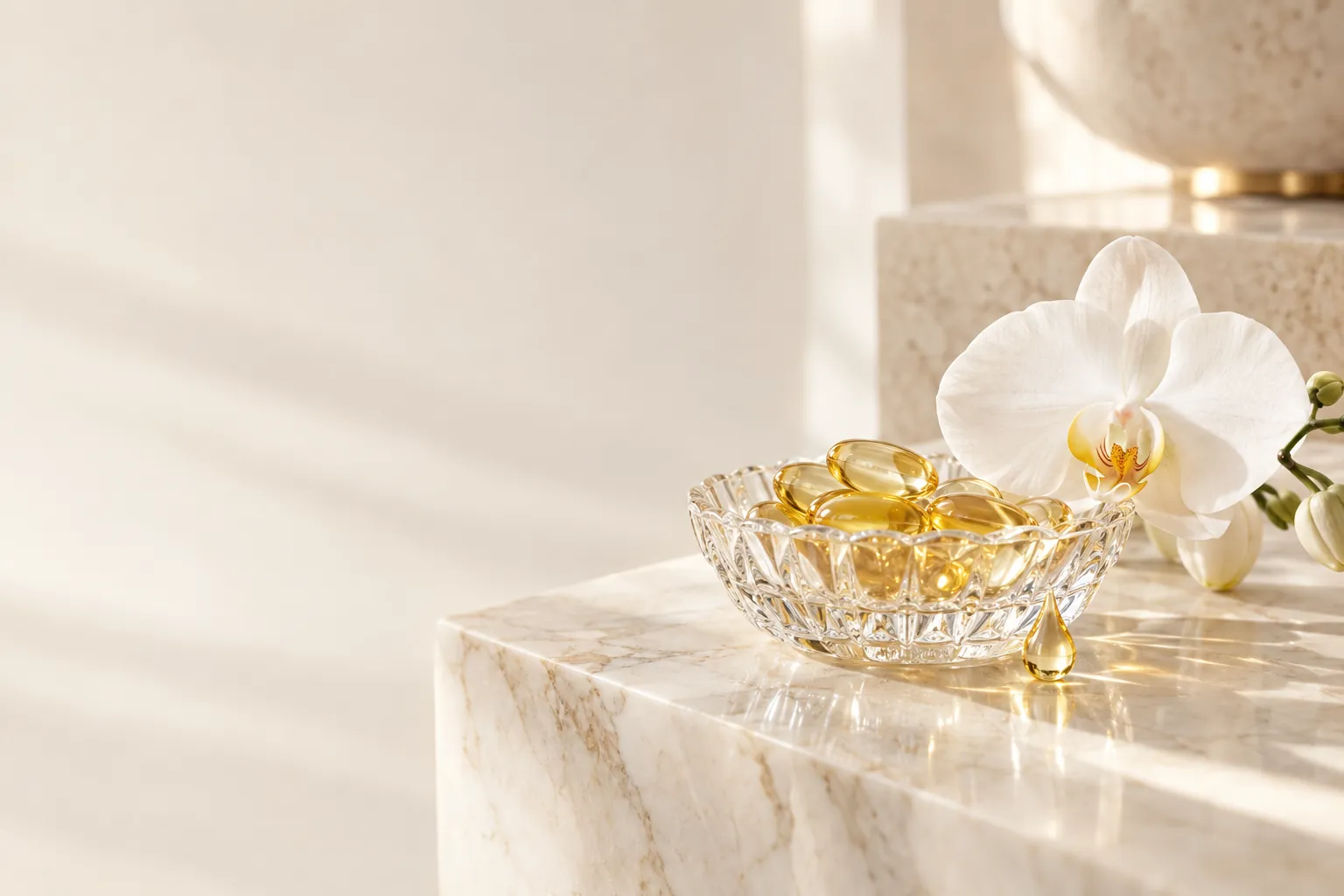 A crystal dish of golden omega capsules beside a white orchid on cream marble