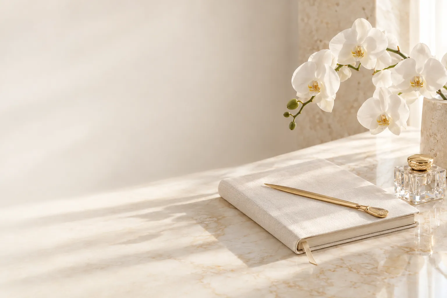 An ivory journal and gold letter opener on cream marble beside a white orchid